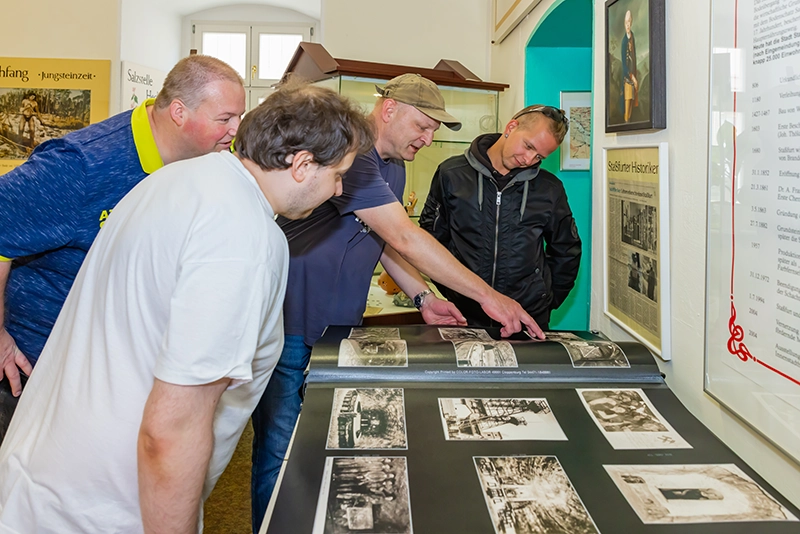 Vier Männer betrachten Schwarz-Weiß-Fotos an einer Ausstellungstafel